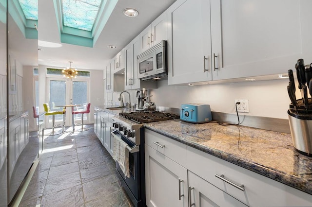 kitchen with stone counters, sink, a skylight, white cabinetry, and stainless steel appliances