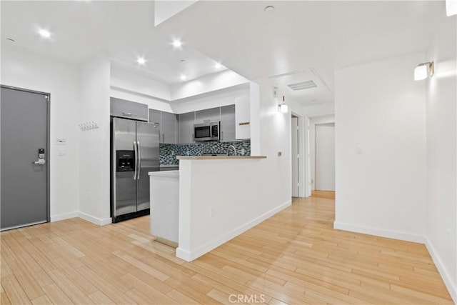 kitchen with kitchen peninsula, light wood-type flooring, stainless steel appliances, and gray cabinetry