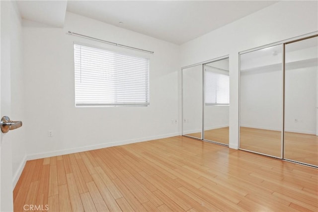 unfurnished bedroom with multiple windows, hardwood / wood-style floors, and two closets