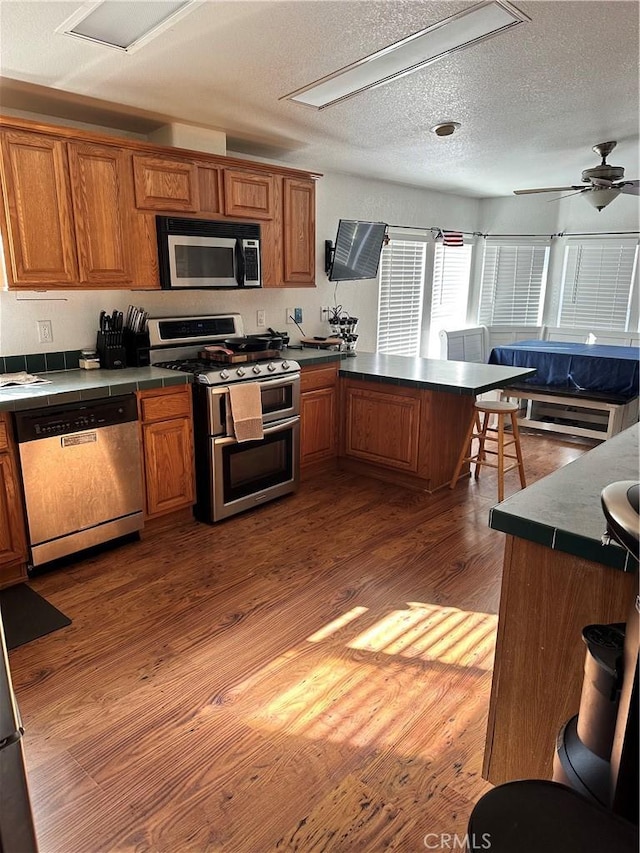 kitchen featuring hardwood / wood-style floors, ceiling fan, a textured ceiling, appliances with stainless steel finishes, and a breakfast bar area