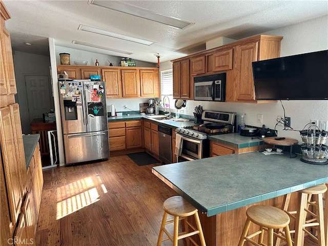 kitchen with lofted ceiling, dark wood-type flooring, a textured ceiling, appliances with stainless steel finishes, and a kitchen bar