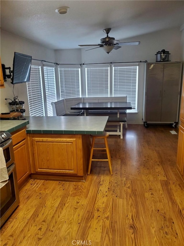 kitchen with tile countertops, ceiling fan, light wood-type flooring, and stainless steel stove