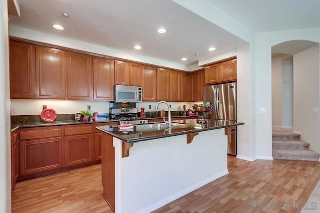 kitchen with sink, stainless steel appliances, an island with sink, a kitchen bar, and light wood-type flooring