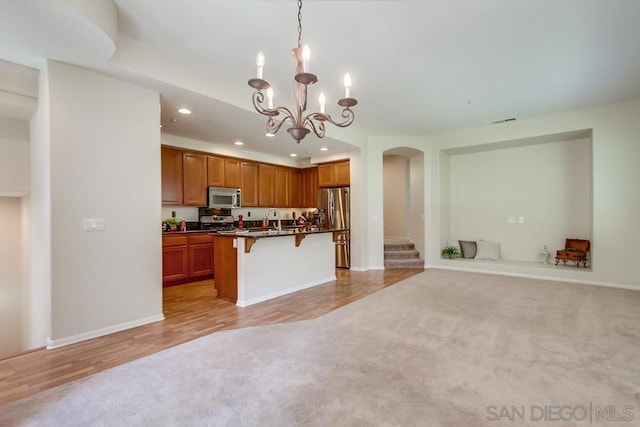 kitchen with a kitchen breakfast bar, stainless steel appliances, a kitchen island with sink, and light hardwood / wood-style flooring