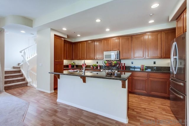 kitchen featuring a kitchen bar, stainless steel fridge, a kitchen island with sink, dark stone countertops, and light hardwood / wood-style floors