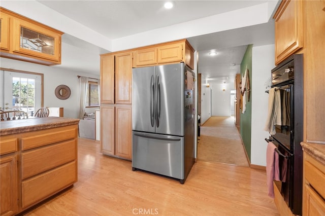 kitchen featuring stainless steel refrigerator, black double oven, light hardwood / wood-style floors, and light brown cabinets