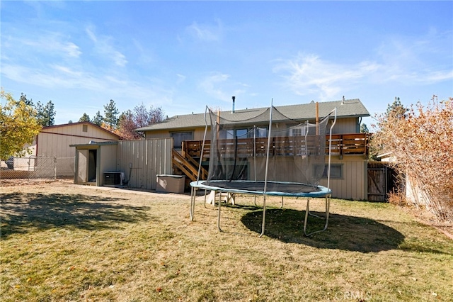 rear view of house with central AC, a yard, a wooden deck, and a trampoline