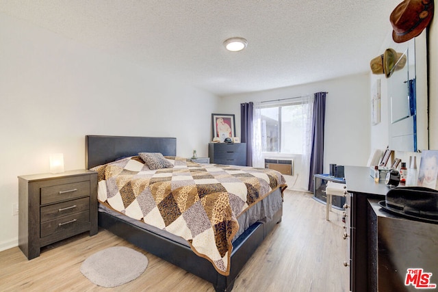 bedroom featuring light hardwood / wood-style floors, a textured ceiling, and an AC wall unit