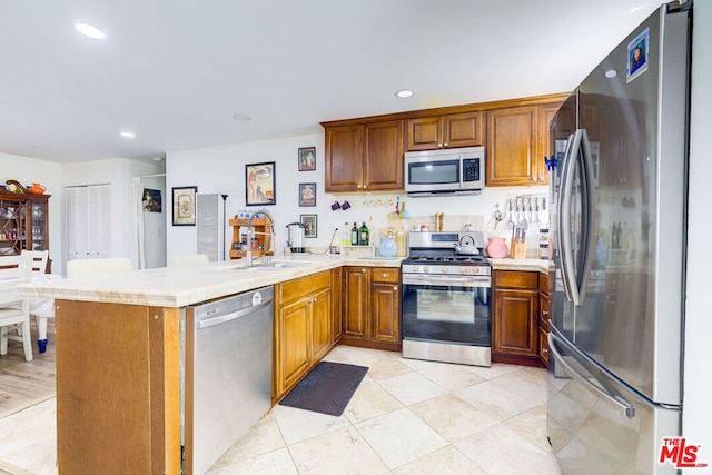 kitchen featuring sink, light tile patterned floors, kitchen peninsula, and appliances with stainless steel finishes