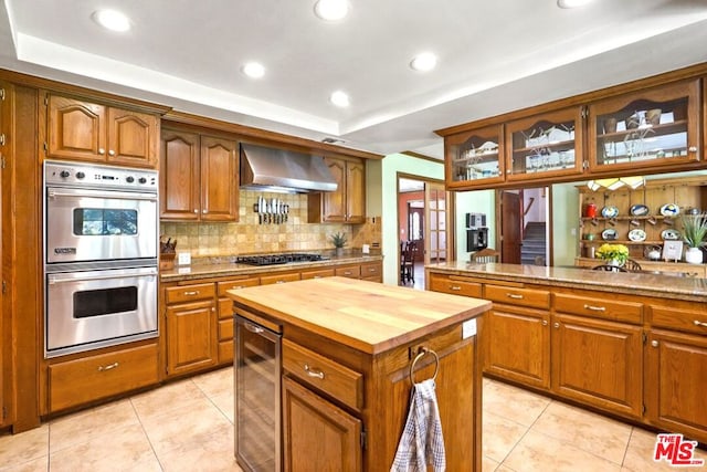 kitchen with wine cooler, wall chimney exhaust hood, light tile patterned floors, a kitchen island, and stainless steel appliances