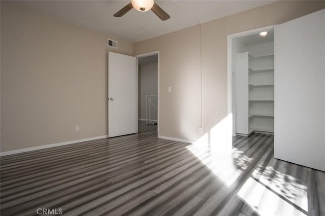 unfurnished bedroom featuring a closet, a spacious closet, dark hardwood / wood-style flooring, and ceiling fan