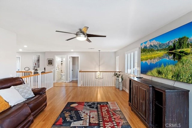 living room featuring ceiling fan with notable chandelier and light hardwood / wood-style flooring