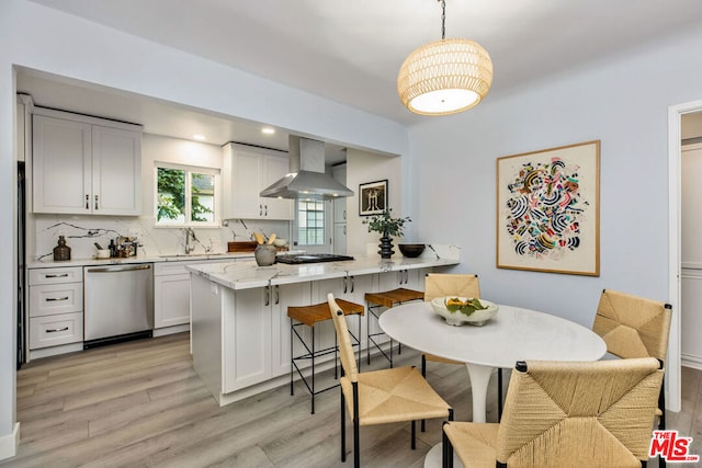 kitchen with pendant lighting, wall chimney range hood, white cabinets, and dishwasher