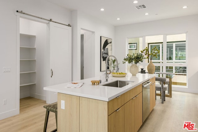 kitchen featuring light wood-type flooring, sink, a barn door, and an island with sink