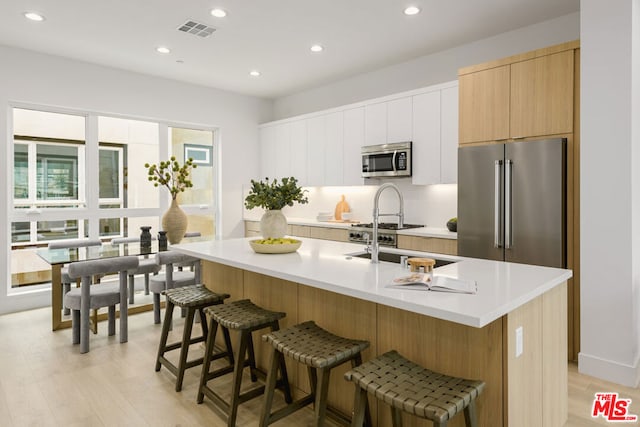 kitchen featuring a center island with sink, white cabinets, light wood-type flooring, a kitchen bar, and stainless steel appliances