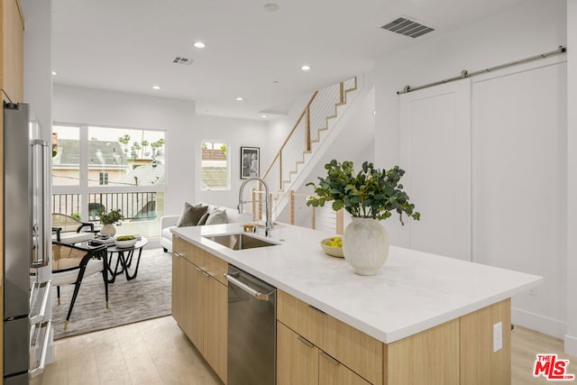 kitchen with sink, a barn door, light hardwood / wood-style floors, a center island with sink, and appliances with stainless steel finishes