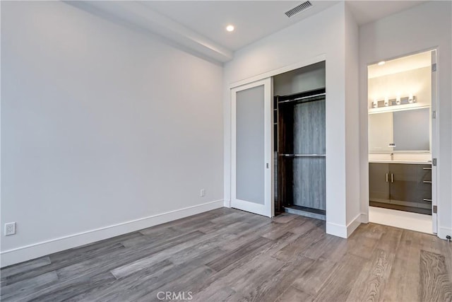 unfurnished bedroom featuring ensuite bath, a closet, and hardwood / wood-style floors