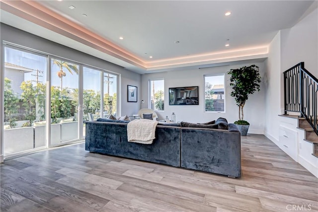 living room with a tray ceiling, light hardwood / wood-style flooring, and plenty of natural light