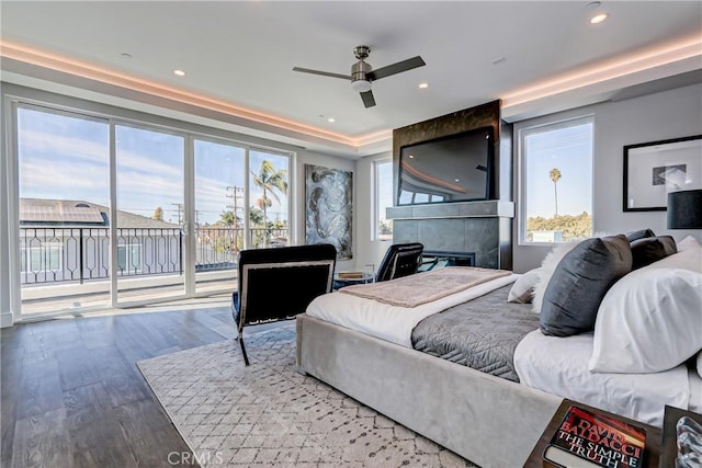 bedroom featuring access to exterior, wood-type flooring, ceiling fan, and a tiled fireplace