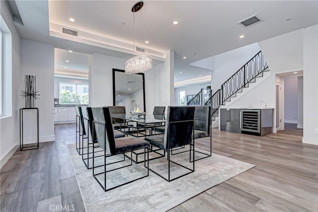 dining space with wine cooler, a notable chandelier, light hardwood / wood-style floors, indoor bar, and a tray ceiling