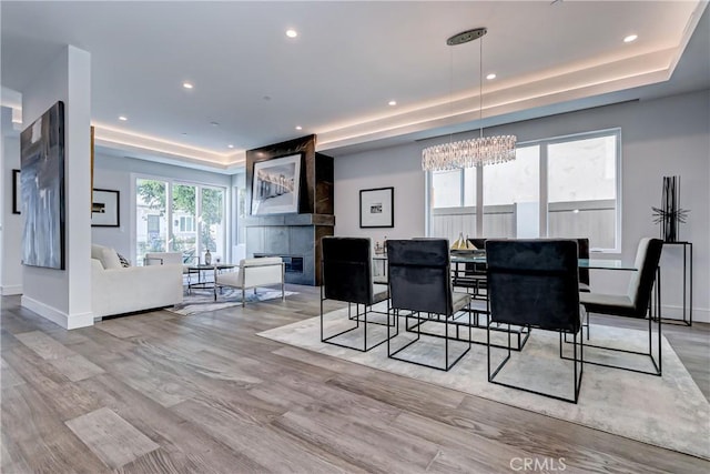 dining area featuring a raised ceiling, a fireplace, light hardwood / wood-style flooring, and a notable chandelier