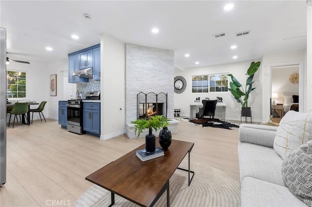 living room with ceiling fan, a healthy amount of sunlight, light wood-type flooring, and a fireplace