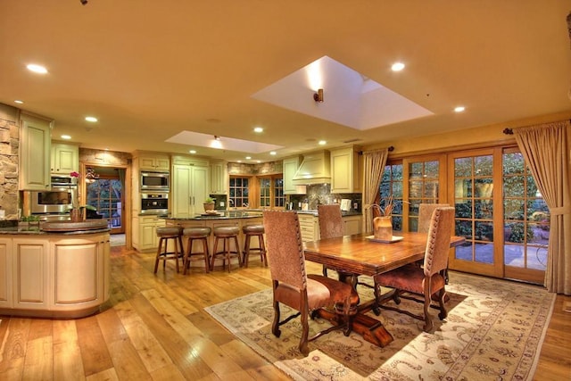 dining space featuring a raised ceiling, light hardwood / wood-style flooring, and french doors