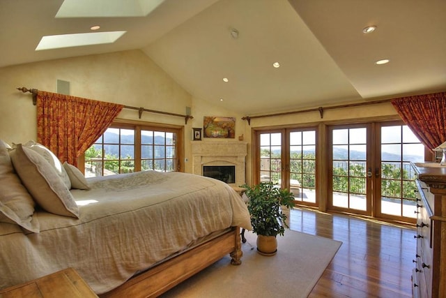 bedroom with multiple windows, vaulted ceiling with skylight, wood-type flooring, and access to exterior