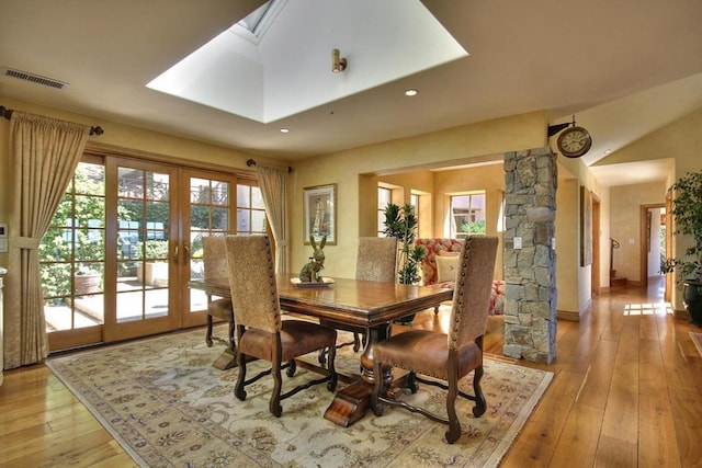 dining space with ornate columns, light wood-type flooring, french doors, and a skylight