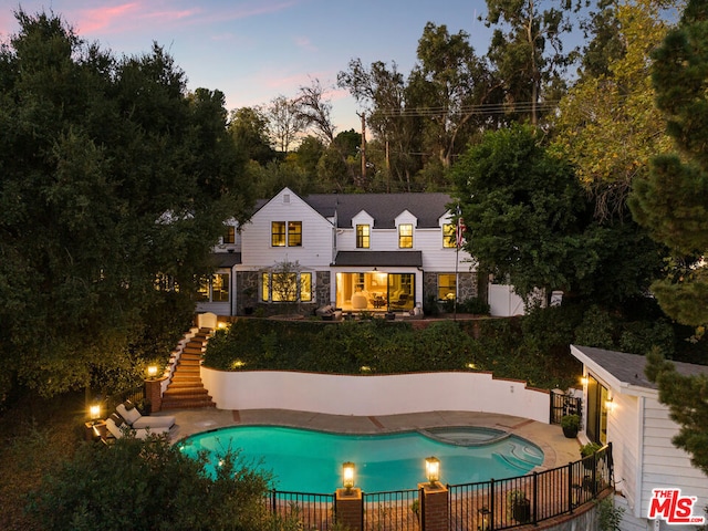 back house at dusk with a pool with hot tub and a patio area