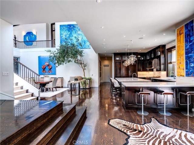 bar with dark wood-type flooring, an inviting chandelier, sink, stainless steel range oven, and dark brown cabinetry