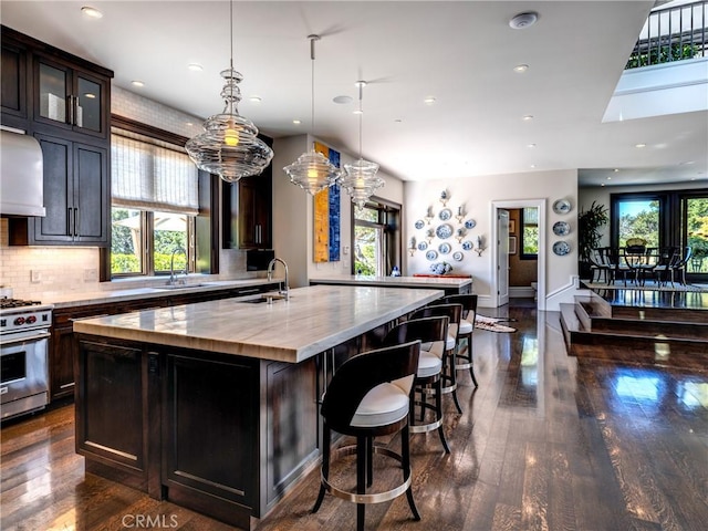 kitchen with high end range, dark hardwood / wood-style floors, an island with sink, tasteful backsplash, and decorative light fixtures