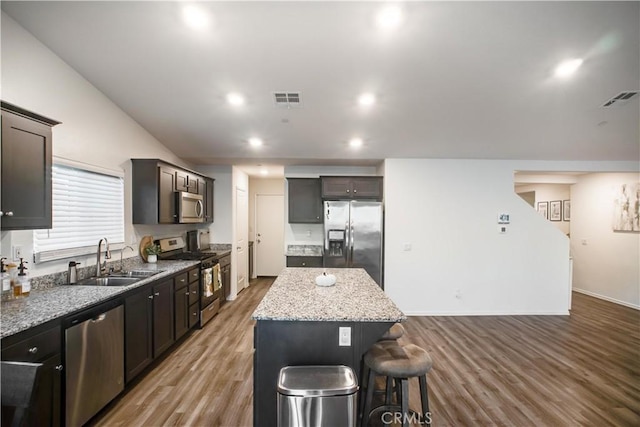 kitchen with sink, stainless steel appliances, a breakfast bar, a kitchen island, and hardwood / wood-style flooring