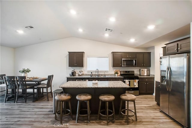 kitchen with a kitchen breakfast bar, sink, vaulted ceiling, a kitchen island, and stainless steel appliances