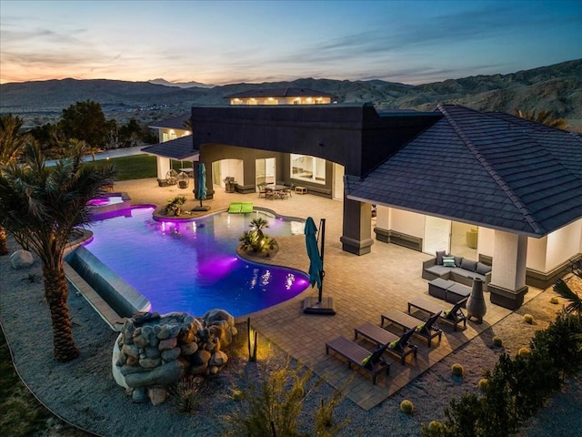 pool at dusk featuring a mountain view, an outdoor living space, and a patio