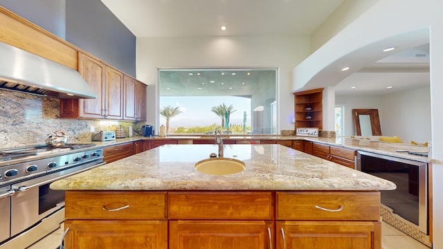 kitchen featuring a center island with sink, beverage cooler, light stone counters, and high end stainless steel range