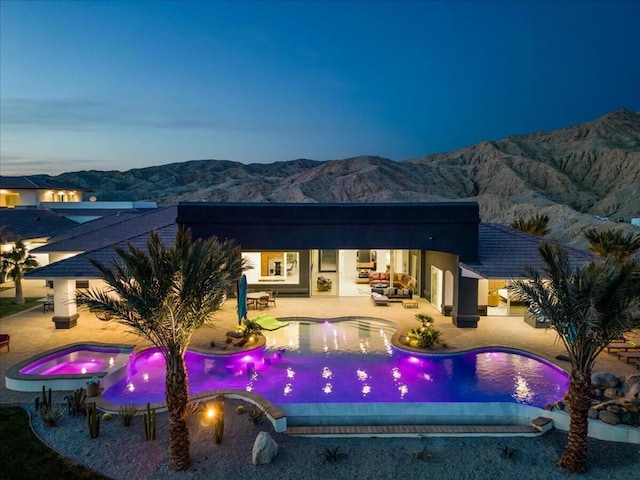 pool at dusk featuring a patio area, an in ground hot tub, and a mountain view