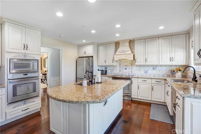 kitchen with appliances with stainless steel finishes, dark hardwood / wood-style flooring, premium range hood, sink, and white cabinetry