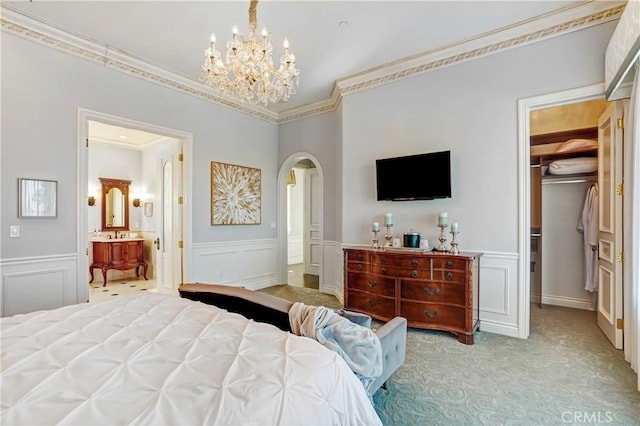 carpeted bedroom with a walk in closet, ornamental molding, an inviting chandelier, connected bathroom, and a closet