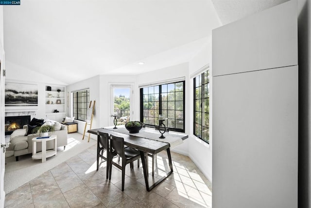 dining space featuring a fireplace, vaulted ceiling, built in features, and a healthy amount of sunlight