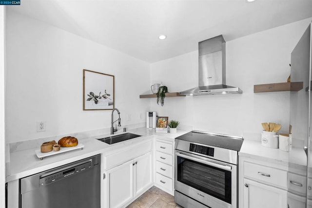 kitchen with appliances with stainless steel finishes, sink, white cabinetry, and wall chimney range hood