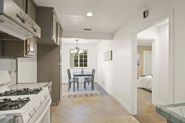 kitchen with pendant lighting, an inviting chandelier, white gas range oven, light tile patterned floors, and dark brown cabinets