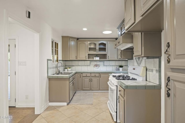 kitchen with sink, white range oven, tile countertops, backsplash, and light tile patterned floors