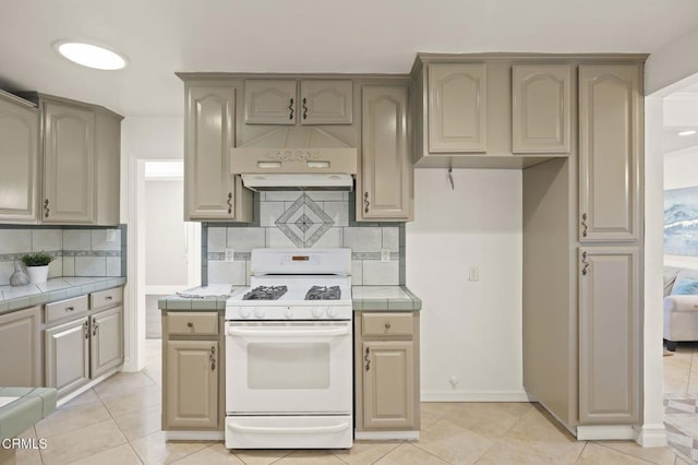 kitchen with light tile patterned floors, white gas range oven, tile countertops, and backsplash