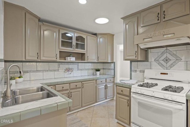 kitchen with tile countertops, sink, light tile patterned floors, tasteful backsplash, and gas range gas stove