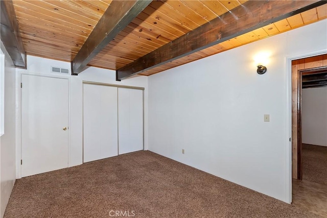 unfurnished bedroom with carpet, beam ceiling, a closet, and wood ceiling