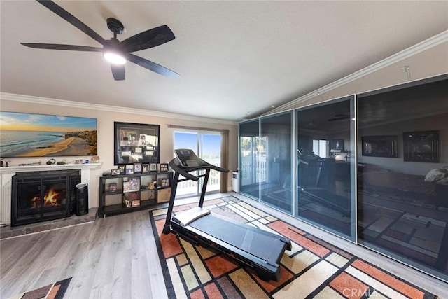 workout area featuring ceiling fan, wood-type flooring, crown molding, and a tile fireplace