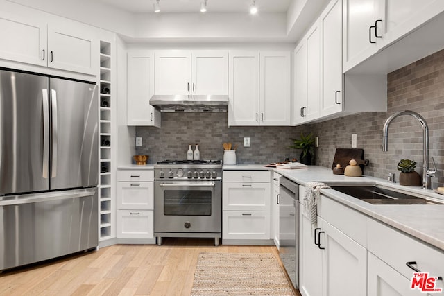 kitchen with sink, light hardwood / wood-style flooring, appliances with stainless steel finishes, tasteful backsplash, and white cabinetry