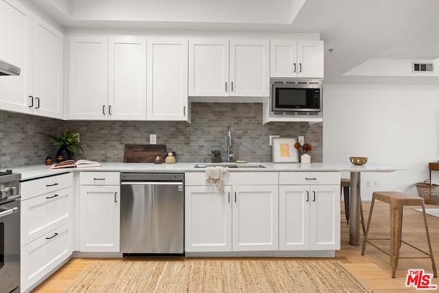 kitchen with light hardwood / wood-style floors, white cabinetry, sink, and appliances with stainless steel finishes