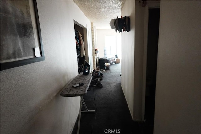 hallway with dark carpet and a textured ceiling